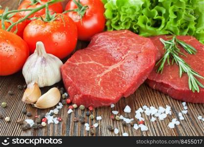 Raw beef steak on cutting board with vegetables and spices on brown wooden background. Beef steak, tomato, salad, garlic, rosemary, spice.. Raw beef steak with vegetables and spices