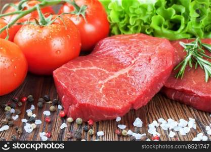 Raw beef steak on cutting board with vegetables and spices on brown wooden background. Beef steak, tomato, salad, garlic, rosemary, spice.. Raw beef steak with vegetables and spices