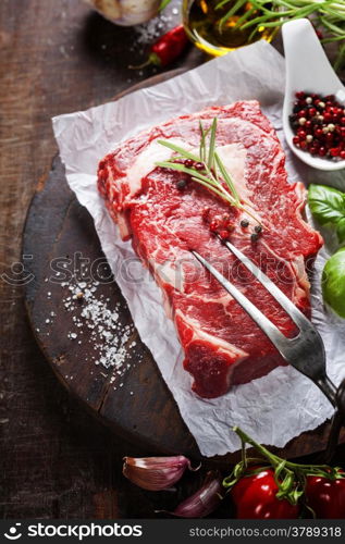 Raw beef steak with meat fork and ingredients on wooden background