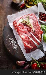 Raw beef steak with meat fork and ingredients on wooden background