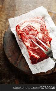 Raw beef steak with meat fork on a an old wooden table