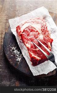 Raw beef steak with meat fork on a an old wooden table