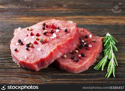 raw beef steak with rosemary and spice on brown wooden background. raw beef steak with rosemary on brown wooden background