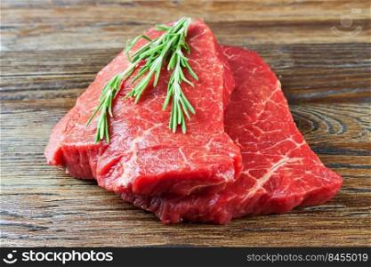 raw beef steak with rosemary on brown wooden background. raw beef steak with rosemary