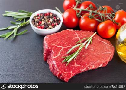 Raw beef steak with sπces and ingredients for cooking on black slate background. Mockup with©space for text. Raw steak with cooking ingridients on black slate background