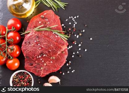 Raw beef steak with spices and ingredients for cooking on black slate background. Top view, flat lay, mockup with copy space for text. Raw steak with cooking ingridients on black slate background