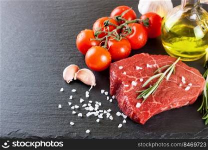 Raw beef steak with spices and ingredients for cooking on black slate background. Mockup with copy space for text. Raw steak with cooking ingridients on black slate background