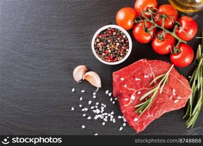 Raw beef steak with spices and ingredients for cooking on black slate background. Top view, flat lay, mockup with copy space for text. Raw steak with cooking ingridients on black slate background