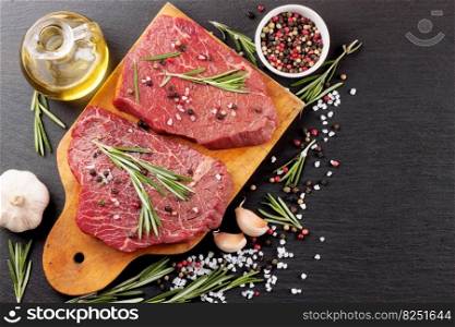Raw beef steak with spices and ingredients for cooking on cutting borard and slate background. Top view.. raw beef steak with spice