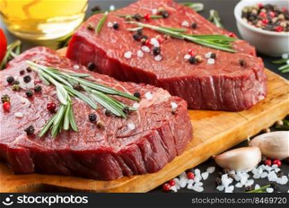 Raw beef steak with spices and ingredients for cooking on cutting borard and slate background. Top view.. Fresh raw beef steak with spice on black slate background