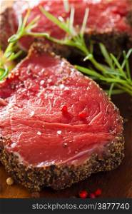 raw beef steak with spices and rosemary on wooden background