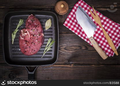 raw beef steak with spices on a black frying pan, next knife, top view, empty space in the middle