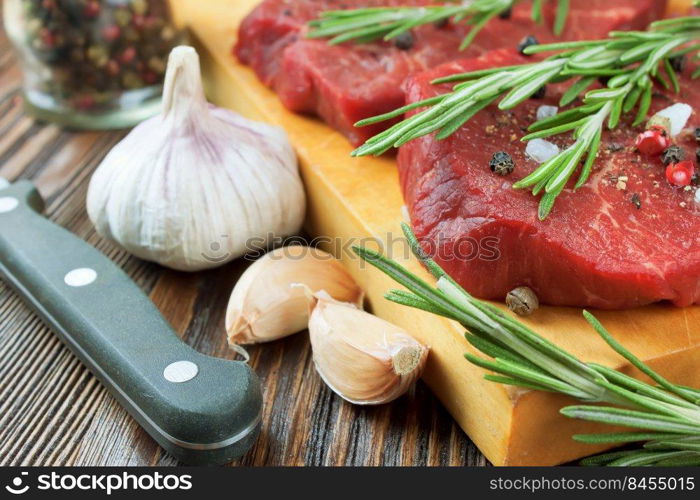 Raw beef steak with vegetables and spices on cuting board and brown wooden background. Beef steak, garlic, spice, rosemary, knife.. Raw beef steak with vegetables and spices