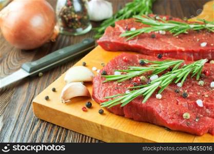 Raw beef steak with vegetables and spices on cuting board and brown wooden background. Beef steak, garlic, spice, rosemary, knife.. Raw beef steak with vegetables and spices