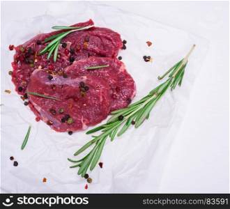 raw beef steaks with spices and rosemary on white paper, empty space on the right