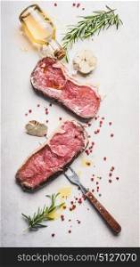 Raw beef Striploin steaks with oil , spices and meat fork on white stone background, top view, flat lay, vertical