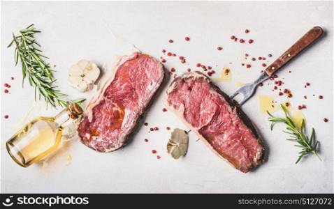 Raw beef Striploin steaks with oil , spices and meat fork on white stone background, top view, flat lay, horizontal