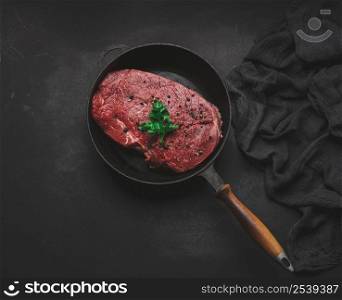 Raw beef tenderloin lies in a metal round frying pan on a black table, top view