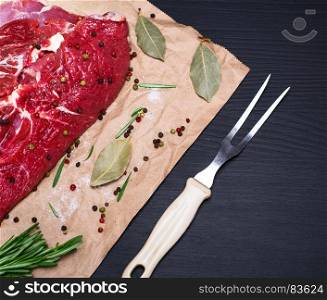 raw beef tenderloin on brown kraft paper and a kitchen fork on a black background, empty space on the right