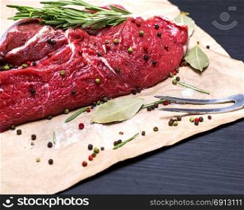 raw beef tenderloin on brown kraft paper and a kitchen fork on a black background