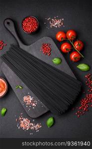 Raw black spaghetti pasta with tomatoes, salt, spices and herbs on a dark concrete background. Raw black spaghetti pasta with tomatoes, salt, spices and herbs