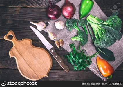 raw broccoli, onion, garlic and parsley on a gray textile napkin, next to a wooden cutting board