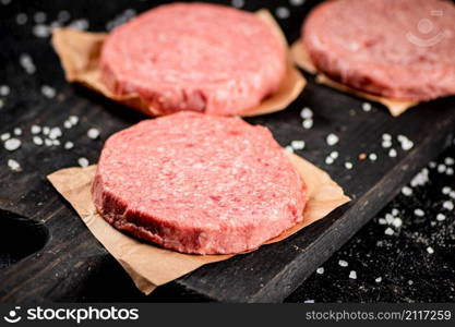 Raw burger on a cutting board. On a black background. High quality photo. Raw burger on a cutting board.