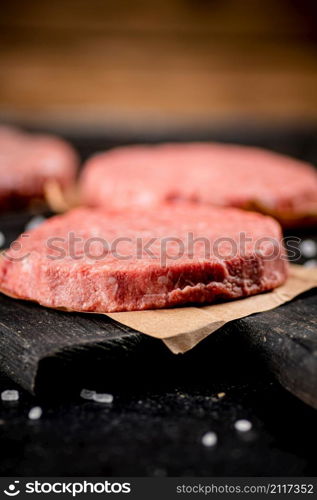 Raw burger on a cutting board. On a black background. High quality photo. Raw burger on a cutting board.