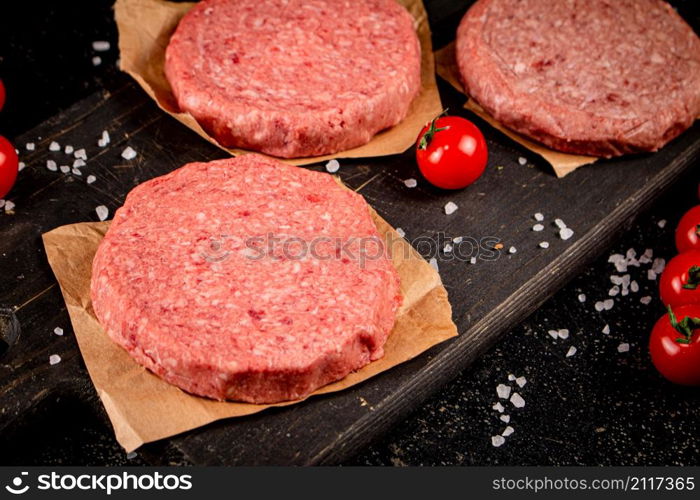 Raw burger on a cutting board. On a black background. High quality photo. Raw burger on a cutting board.