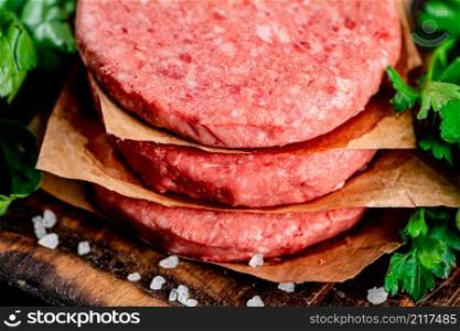 Raw burger on a cutting board with parsley and salt. Macro background. High quality photo. Raw burger on a cutting board with parsley and salt.