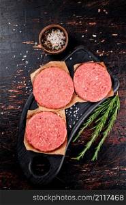 Raw burger on a cutting board with rosemary. On a rustic dark background. High quality photo. Raw burger on a cutting board with rosemary.