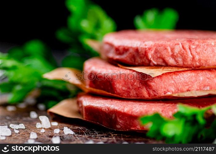 Raw burger on a table with greens and salt. On a black background. High quality photo. Raw burger on a table with greens and salt.