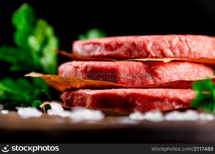 Raw burger on a table with greens and salt. On a black background. High quality photo. Raw burger on a table with greens and salt.