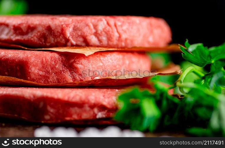 Raw burger on a table with greens and salt. On a black background. High quality photo. Raw burger on a table with greens and salt.