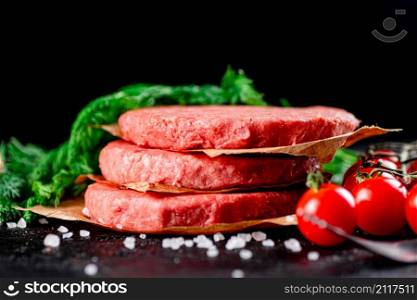 Raw burger on a table with greens and salt. On a black background. High quality photo. Raw burger on a table with greens and salt.