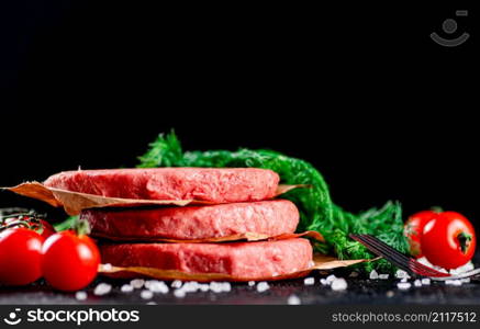 Raw burger on a table with greens and salt. On a black background. High quality photo. Raw burger on a table with greens and salt.