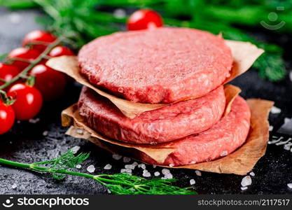 Raw burger on a table with greens and salt. On a black background. High quality photo. Raw burger on a table with greens and salt.