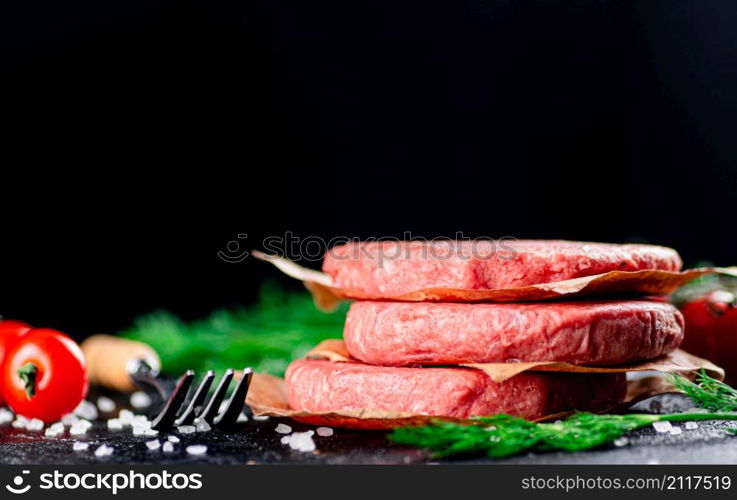 Raw burger on a table with greens and salt. On a black background. High quality photo. Raw burger on a table with greens and salt.