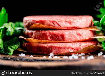 Raw burger on a wooden cutting board with parsley. On a black background. High quality photo. Raw burger on a wooden cutting board with parsley.