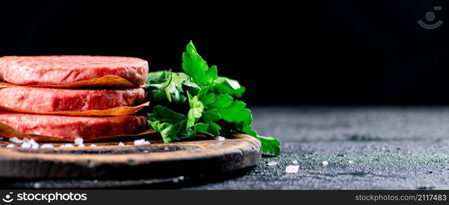 Raw burger on a wooden cutting board with parsley. On a black background. High quality photo. Raw burger on a wooden cutting board with parsley.