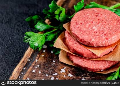Raw burger on a wooden cutting board with parsley. On a black background. High quality photo. Raw burger on a wooden cutting board with parsley.