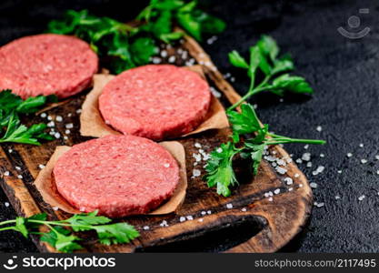 Raw burger on a wooden cutting board with parsley. On a black background. High quality photo. Raw burger on a wooden cutting board with parsley.