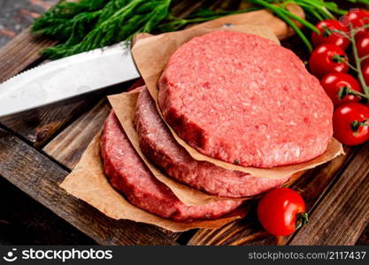 Raw burger on a wooden tray with tomatoes and dill. Against a dark background. High quality photo. Raw burger on a wooden tray with tomatoes and dill.