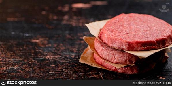 Raw burger on paper. On a rustic dark background. High quality photo. Raw burger on paper. On a rustic dark background.