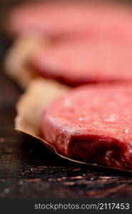 Raw burger on paper. On a rustic dark background. High quality photo. Raw burger on paper. On a rustic dark background.