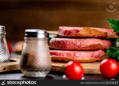 Raw burger with tomatoes and parsley. Against a dark background. High quality photo. Raw burger with tomatoes and parsley.