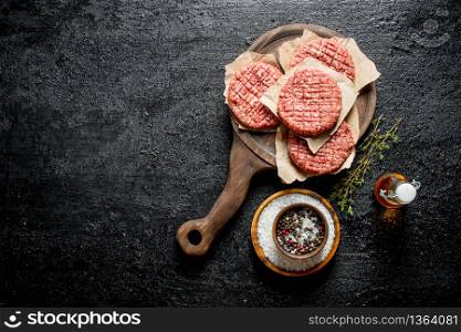 Raw burgers on a cutting Board with spices, oil and thyme. On black rustic background. Raw burgers on a cutting Board with spices, oil and thyme.
