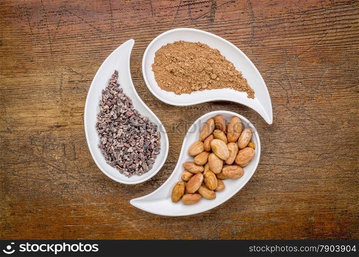 raw cacao beans, nibs and powder - top view of teardrop shaped bowls against rustic wood