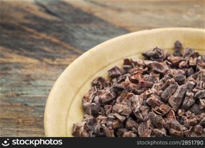 Raw cacao nibs in a small ceramic bowl against grunge wooden background