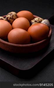 Raw chicken and quail eggs in a brown ceramic bowl on a dark concrete background. Easter preparations